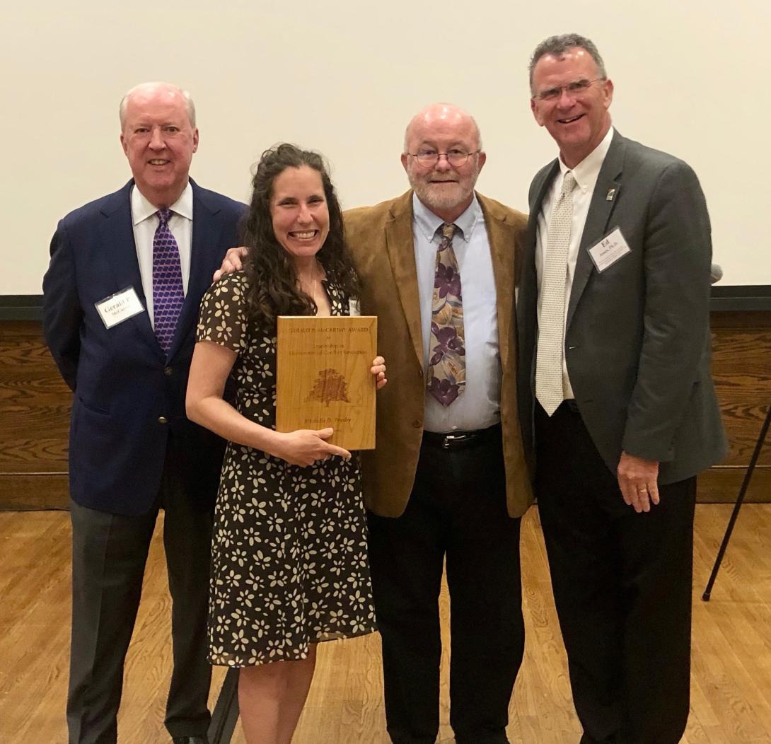 Michelle Prysby receives an award. (Woman holds plaque next two three men)